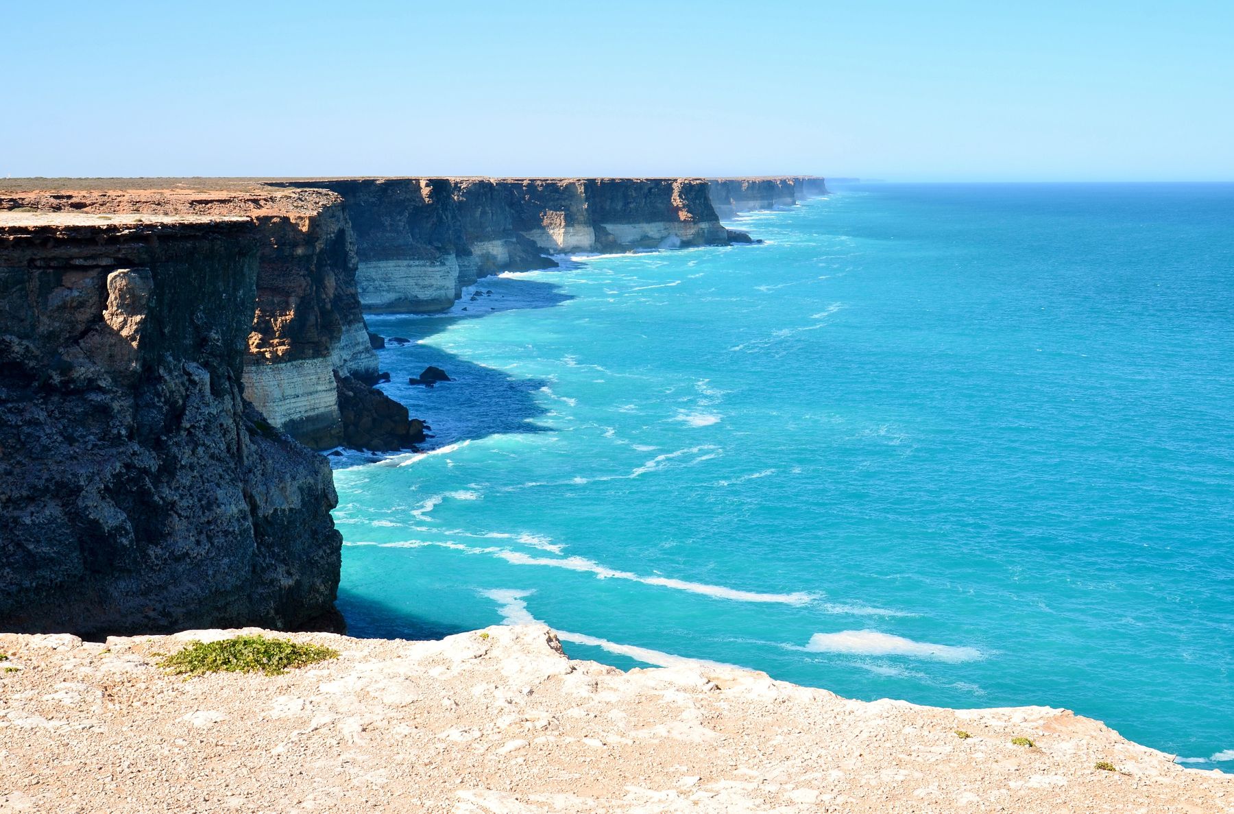 Sheer pale limestone cliffs drop straight into turquoise sea, receding in a long straight line to the horizon under a clear sky.