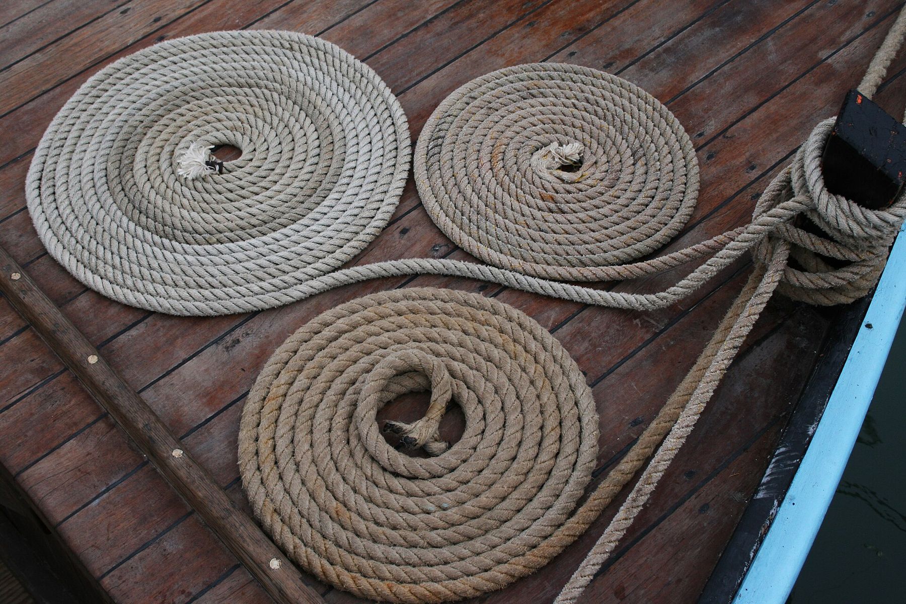 Three flat spirals of tan rope on a varnished wooden deck, with another line wound around a post at the edge of the boat.