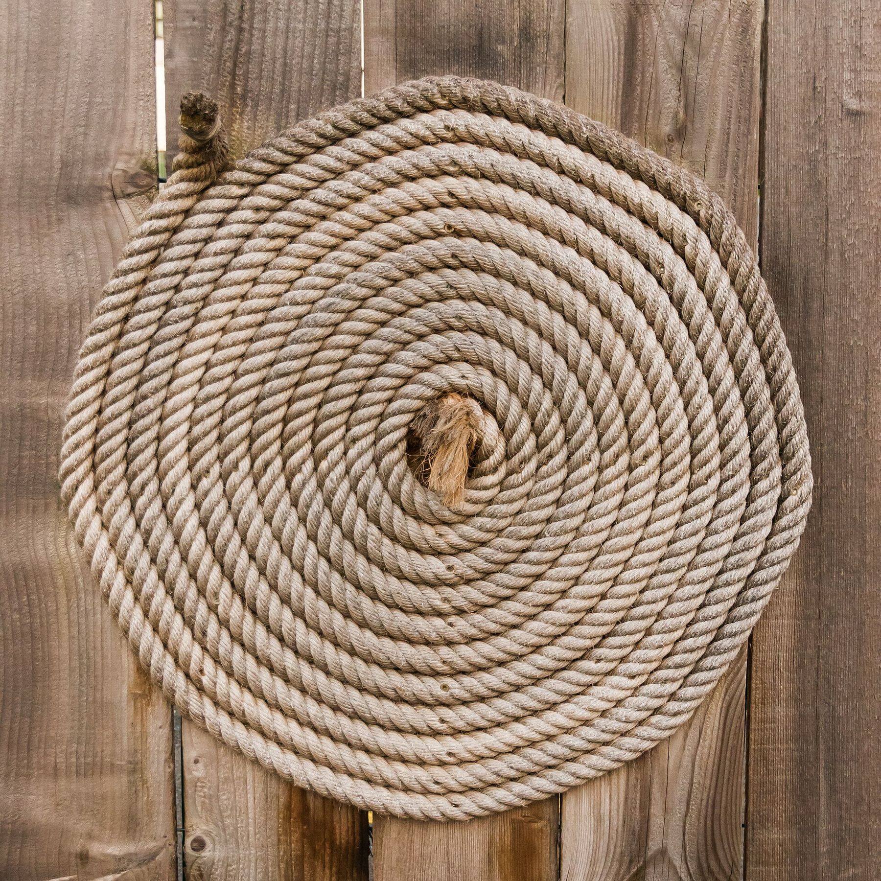 A flat spiral coil of thick tan hemp rope against weathered wooden planks.