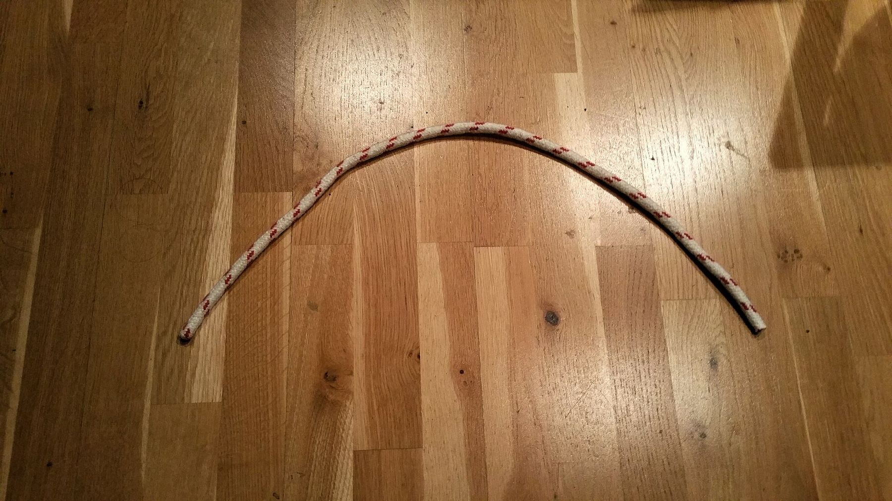 A thin white cord with a red fleck laid across light oak floorboards in a wide, shallow arch.