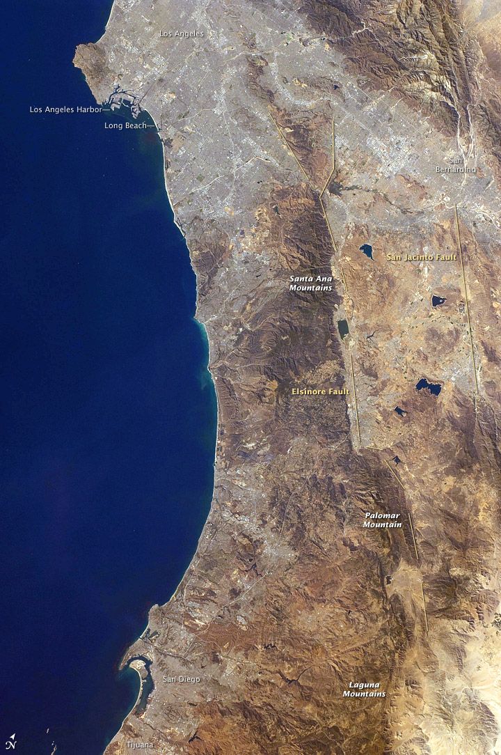 A view from orbit of a dry tan coast running top to bottom beside deep blue ocean, with small printed place labels on the land.